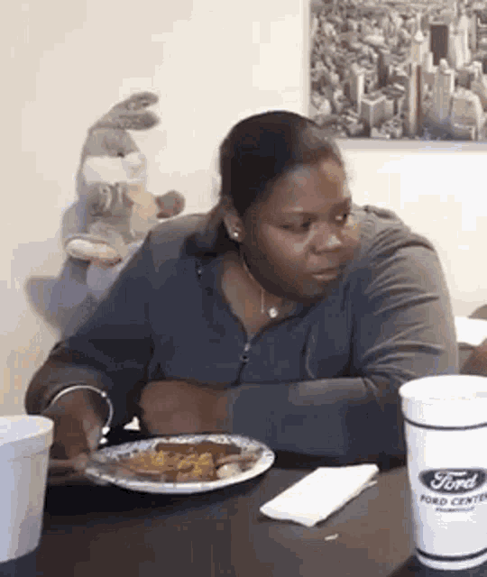 a woman is sitting at a table with a plate of food and a cup that says ford center .