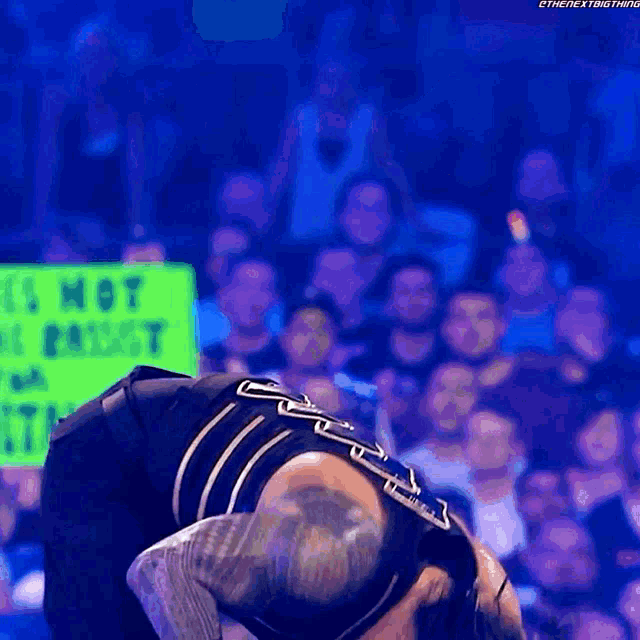 a wrestler is kneeling down in front of a crowd while holding a sign that says it 's not a priest