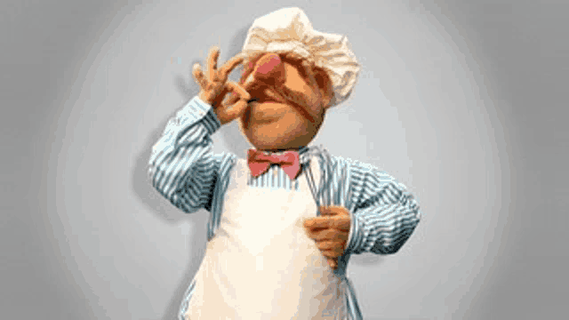 a muppet wearing a chef 's hat and apron with a pink bow tie