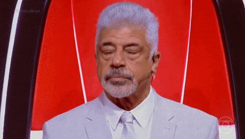 a man with gray hair and a beard stands in front of a red wall with the word brasil on it