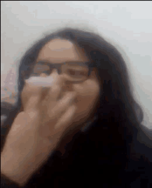 a woman wearing glasses is blowing her nose with her hand