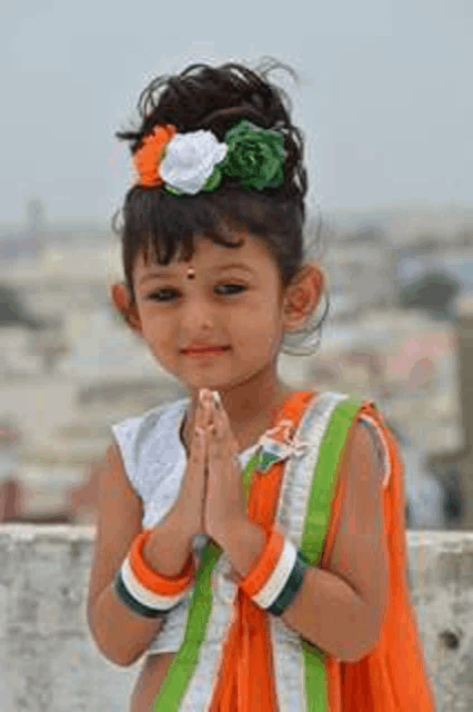 a little girl wearing a patriotic costume is standing with her hands folded .