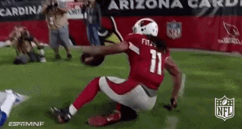 a football player with the number 11 on his jersey is kneeling on the field while holding a football .