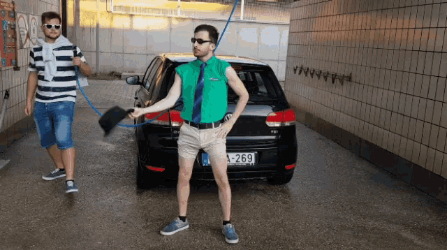 a man in a green shirt and tie stands in front of a black car with a license plate that says 269