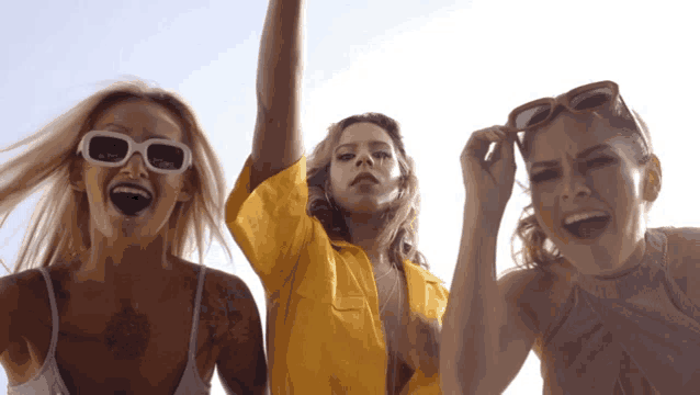 three women wearing sunglasses and a yellow shirt are laughing together