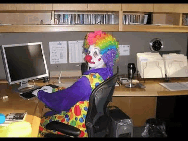 a clown is sitting at a desk with a computer and a keyboard .