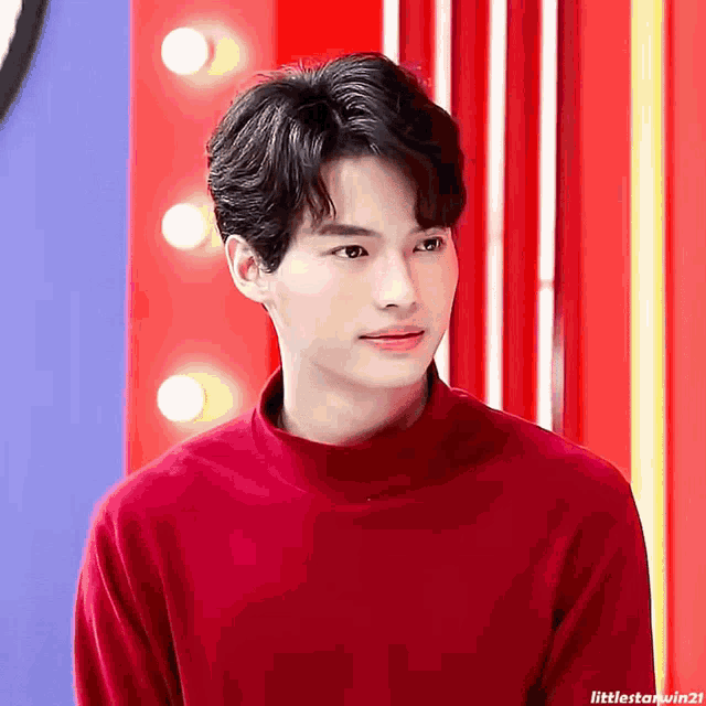 a young man wearing a red turtleneck sweater looks at the camera