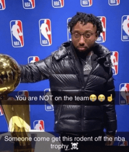 a man in a black jacket holds a trophy in front of a wall with nba logos on it