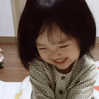 a little girl is sitting on a bed smiling and looking at the camera .