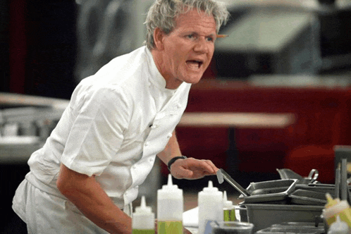 a man in a white chef 's uniform is standing in front of bottles of sauces