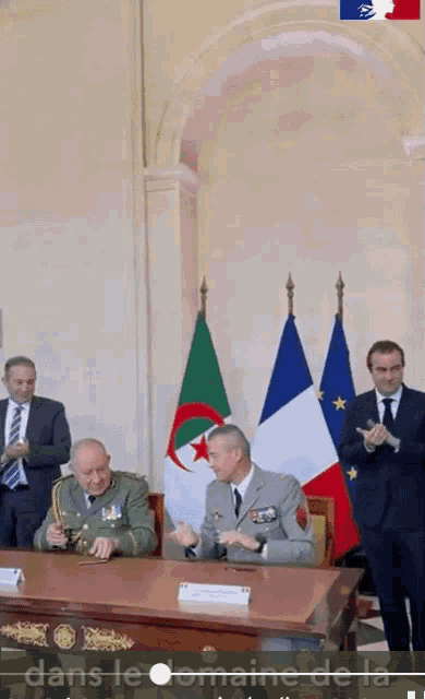 a group of men are sitting at a table with flags in the background and the words dans le domaine de la