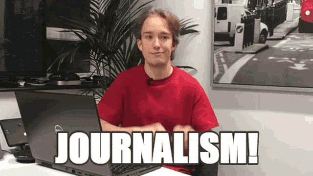 a man in a red shirt is sitting at a desk with a dell laptop and the word journalism written on it