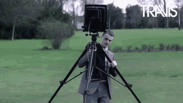 a man in a suit is taking a picture with a camera on a tripod in a field with the word trans in the background