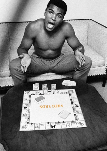 a shirtless man sits on a couch playing a board game called sregairos