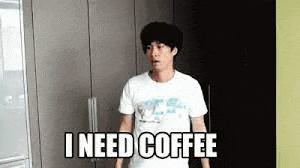 a man in a white t-shirt is standing in a kitchen and says `` i need coffee '' .