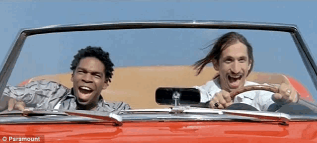 two men are laughing while driving a red car with paramount written on the bottom