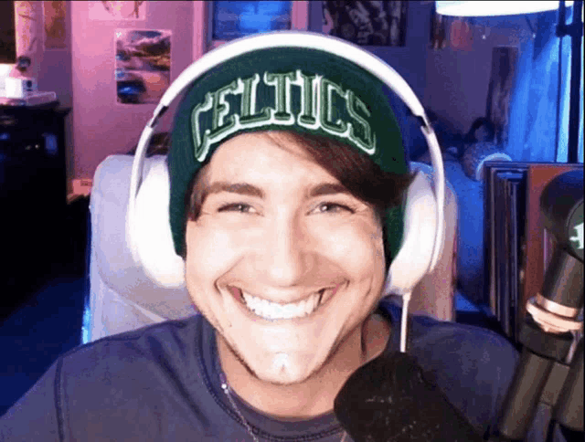 a man wearing headphones and a celtics beanie smiles for the camera