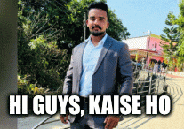 a man in a suit is standing in front of a sign that says " hi guys kaise ho "