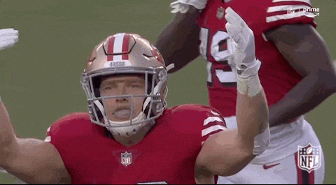 a football player wearing a helmet and gloves is standing on a field with his hands in the air .