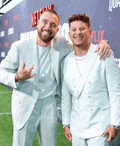 two men in suits are posing for a picture on a red carpet .