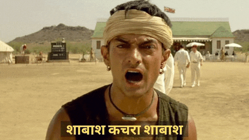 a man wearing a turban and a necklace is screaming in front of a building in a field .