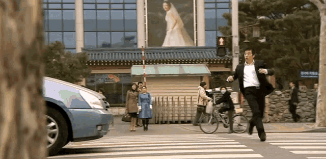 a man in a suit is running across a crosswalk in front of a building with a sign that says ' korean '