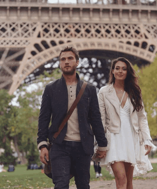 a man and a woman walking in front of the eiffel tower