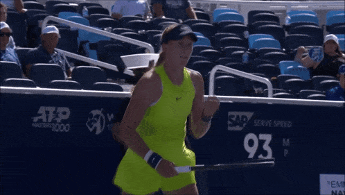 a woman in a neon yellow dress is holding a tennis racquet in front of a sign that says 93