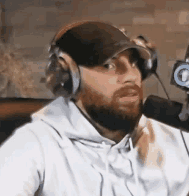 a man with a beard is wearing headphones and a baseball cap while talking into a microphone .