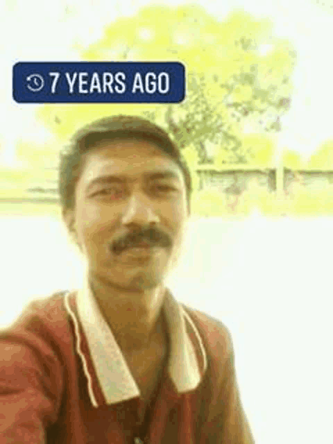 a man with a mustache is taking a selfie in front of a sign that says `` 7 years ago '' .