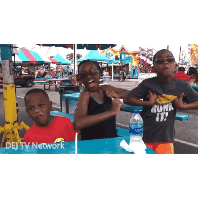 three children are sitting at a table with a bottle of aquafina water between them