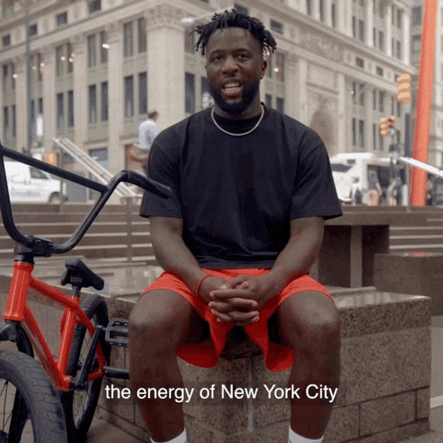 a man sitting next to a red bike with the words the energy of new york city written below him