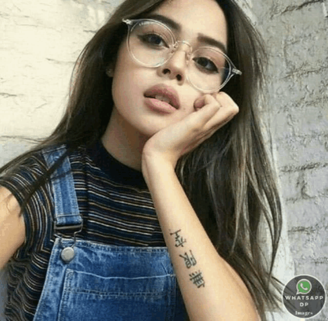 a girl wearing glasses and overalls has a tattoo on her wrist