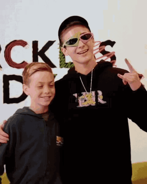 a boy wearing sunglasses stands next to another boy in front of a sign that says rock 'n ' day