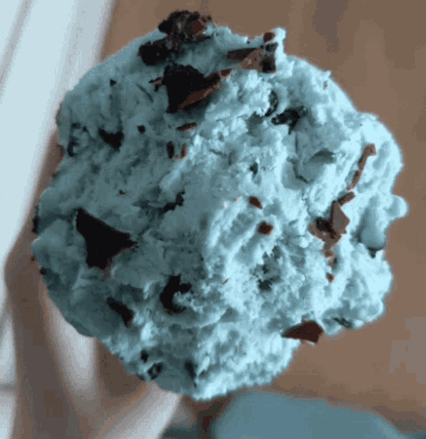 a person is holding a scoop of mint chocolate chip ice cream on a stick