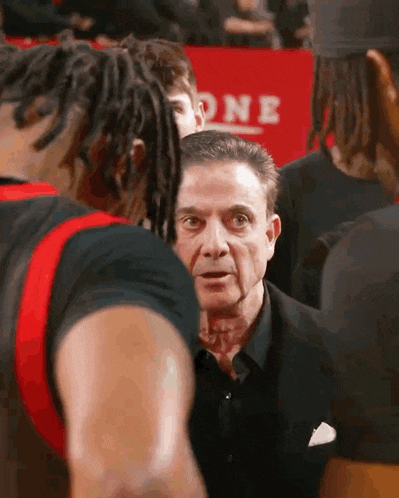 a man in a suit is talking to a group of basketball players in front of a sign that says one