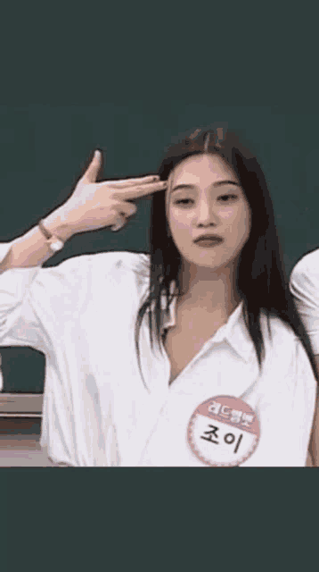 a woman wearing a white shirt and a name tag is making a gun sign with her hands .