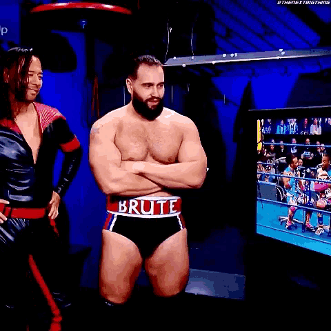 a man with a beard is standing in a locker room with his arms crossed and talking to another man .