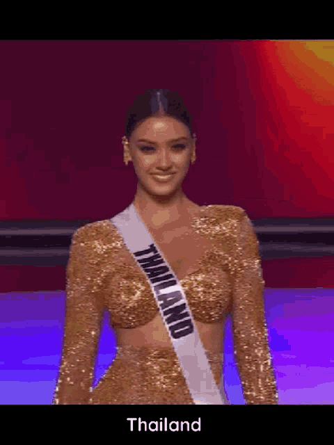 a woman in a gold dress with a sash that says thailand on it is standing on a stage .