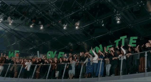 a large group of people standing on a balcony holding up green letters that say " we love eating te "