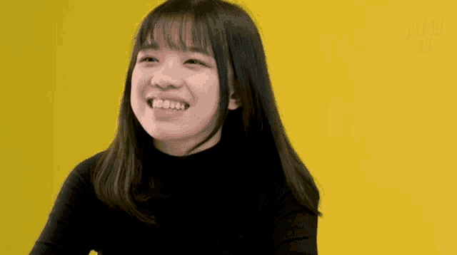 a girl is smiling with a yellow background and the letters jrt are visible in the upper left corner