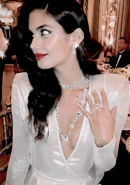 a woman in a white dress is wearing a diamond necklace and earrings