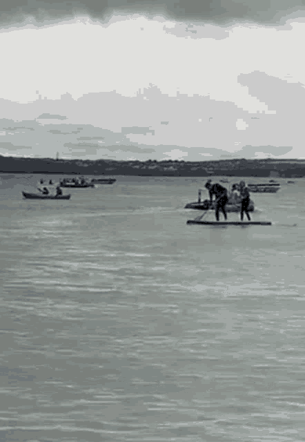 a group of people are standing on a paddle board in the middle of a large body of water .