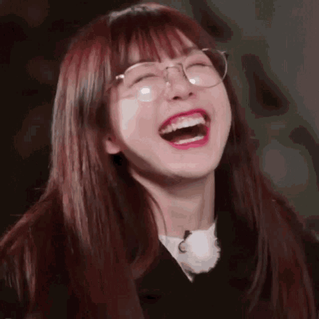 a girl wearing glasses is laughing with her mouth wide open .