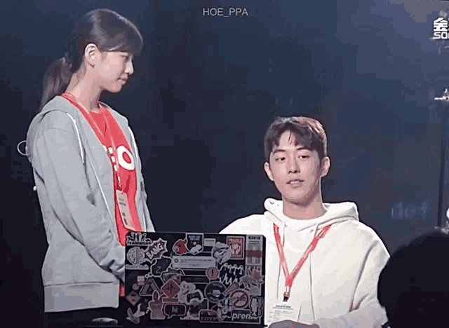 a man and a woman are standing next to each other and the man is holding a laptop that says supreme on it