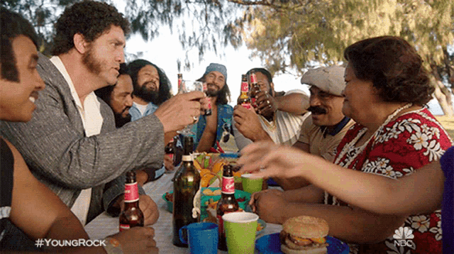 a group of people are sitting around a table with bottles of beer and a nbc logo in the corner