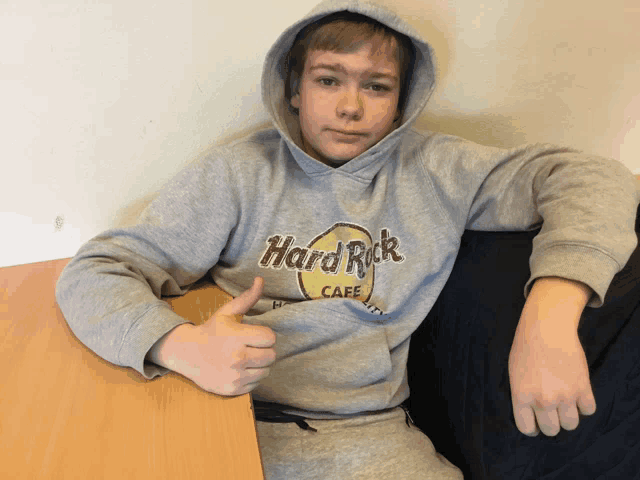 a young boy wearing a grey hard rock cafe hoodie gives a thumbs up