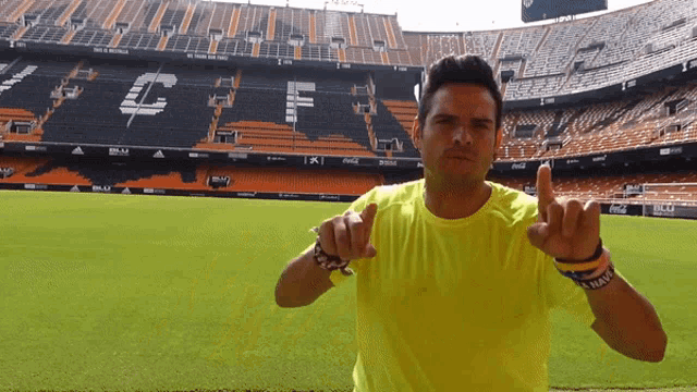 a man in a yellow shirt is pointing at the camera in front of a stadium that has the word coca cola on it