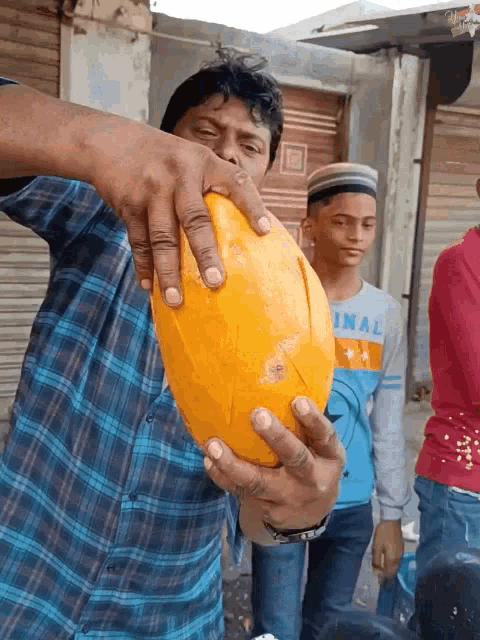 a man in a plaid shirt is holding a large yellow ball and a boy in a blue shirt with the word inal on it