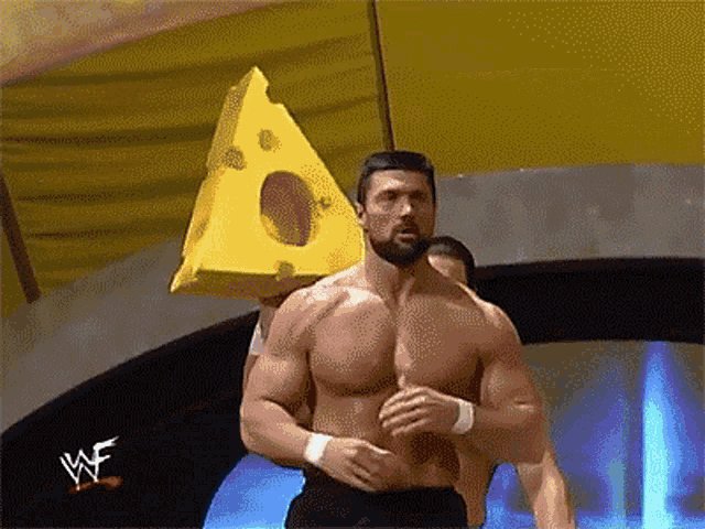 a shirtless wrestler is holding a large piece of cheese